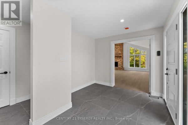 Interior foyer with grey tiled floor, white doors, and an entrance into a living room with a stone fireplace. - 1580 Groves Road, Russell