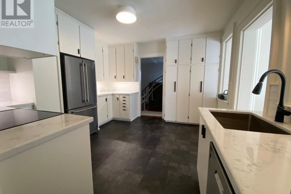White kitchen with stainless steel refrigerator, black faucet, and white cabinets. - 1581 Line 6 Road, Niagara On The Lake