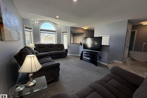 Living room featuring grey carpet, reclining sofas, entertainment center with TV, and access to other rooms. - 15812 133 St Nw, Edmonton