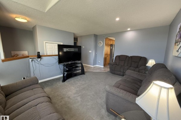 Living room with grey carpet, sofas, TV, and a view into a kitchen and dining area. - 15812 133 St Nw, Edmonton