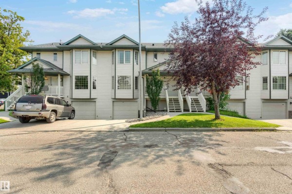 Exterior view of a townhouse with light siding, white trim, and a large tree. - 15817 102 Av Nw, Edmonton