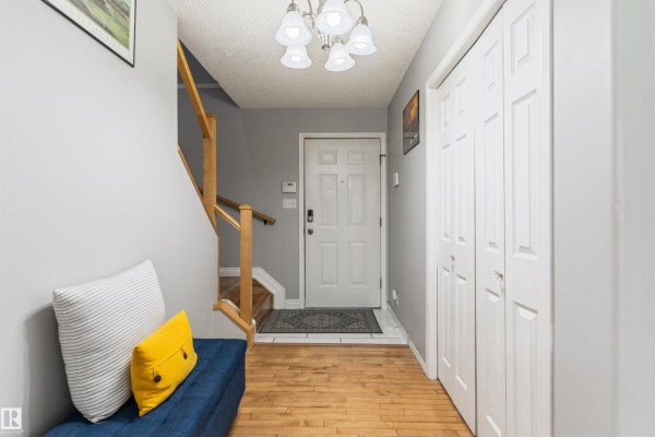 Entrance hallway with wood floor, gray walls, white closet doors, and a bench. - 15817 102 Av Nw, Edmonton