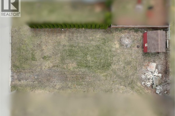 Aerial view of a rectangular lot featuring a red shed, grass, and debris, bordered by a fence and trees. - 1583 Councillors Street, Moore Township