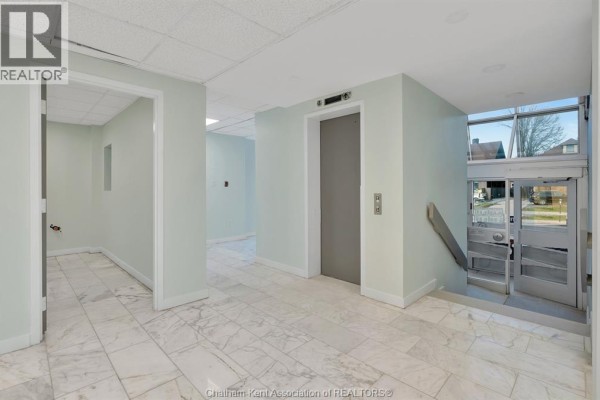 Interior lobby with marble tiled floors, a grey elevator, and a glass entrance door. - 1585 Ouellette Avenue, Windsor