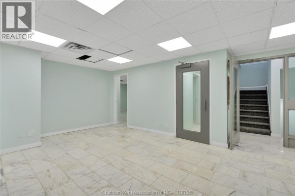 Empty commercial space with light blue walls, marble tiled floors, and a glass door leading to a staircase. - 1585 Ouellette Avenue, Windsor
