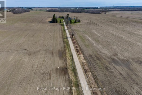 Aerial view of a long dirt road leading through cultivated fields towards a cluster of trees and a building. - 158567 Highway 10, Melancthon