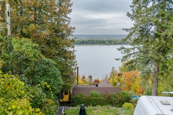 View through trees of a small house and a wide river. - 1587 Lilac Lane, Ottawa