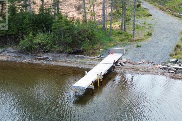 A long wooden dock extends from a gravel shoreline into the calm water. - 1589 Corbetts Cove Road, Barra Head
