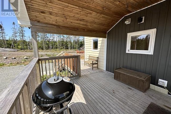 Covered porch with wooden deck, barbecue, seating, and storage box. - 1589 Corbetts Cove Road, Barra Head