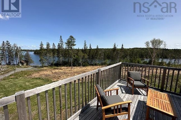 View from a wooden deck of a lake and wooded landscape with chairs and a table. - 1589 Corbetts Cove Road, Barra Head