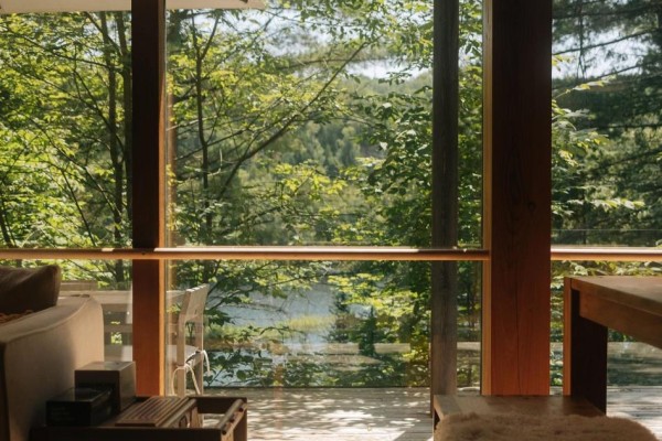 View through large wood-framed windows of trees and a distant body of water. - 158a Ponacka Road, Hastings Highlands