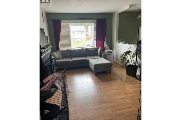 Living room with a sectional sofa, hardwood floors, and a large window overlooking the street. - 159 Gwillim Crescent, Tumbler Ridge