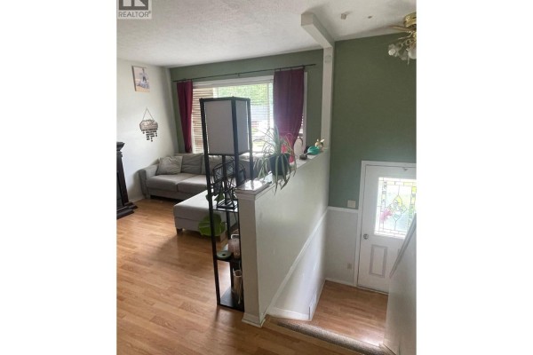 View of the living room and staircase leading down to the front entrance with a stained glass door. - 159 Gwillim Crescent, Tumbler Ridge