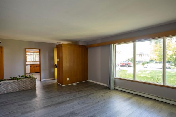 Living room with grey walls, wood paneling, large window, and wood-look flooring. - 159 Larchdale Crescent, Winnipeg
