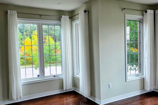 Corner of a room with large bay windows, white curtains, and a view of trees with fall foliage. - 159 Riding Mountain Drive, Richmond Hill