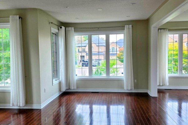 Living room with hardwood floors, large windows, white curtains, and a view of houses across the street. - 159 Riding Mountain Drive, Richmond Hill