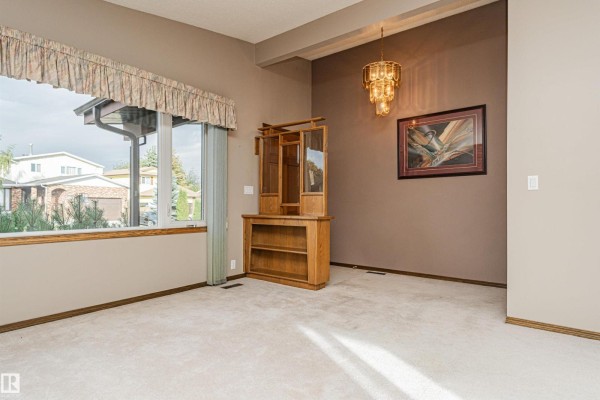 Spacious living area with a chandelier, built-in cabinet, and a large window overlooking the neighborhood. - 15903 111 St Nw, Edmonton