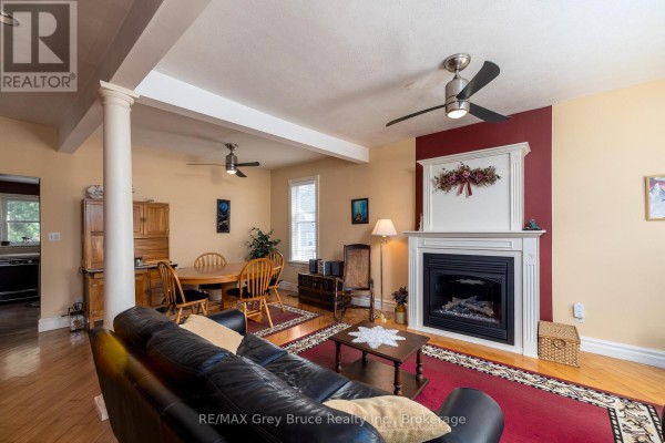 Living room with a black leather sofa, fireplace, and dining area with a wooden table. - 1591 5th Avenue W, Owen Sound
