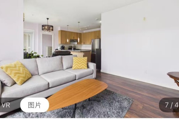 Living room with a grey sectional sofa, yellow accent pillows, and a wood coffee table on a grey rug. - 15918 26 Avenue, Surrey