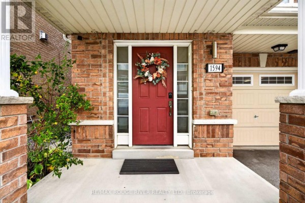 Close-up of the red front door with decorative wreath, brick facade, and porch light. - 1594 Brandy Court, Pickering