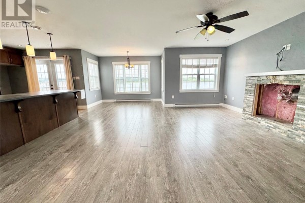 Open concept living area with grey walls, light wood floors, a stone fireplace, and water views. - 15a Main Street, Tilting