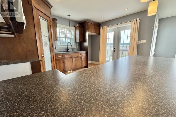 Kitchen with dark wood cabinets, a grey countertop, stainless steel sink, and a view of the back door. - 15a Main Street, Tilting