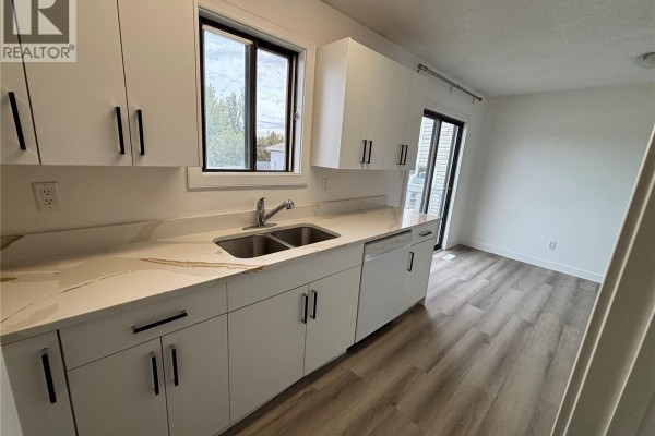 Kitchen with white cabinets, stainless steel sink, dishwasher, and view of dining area. - 15b Erixon Place, Clavet