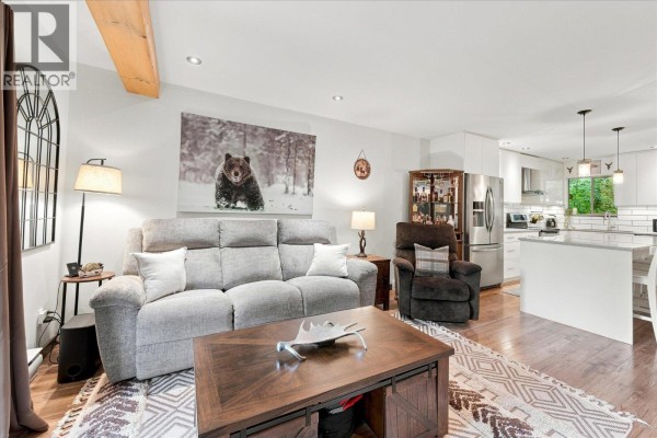 Open-concept living room and kitchen area with a large bear art print and island seating. - 15c 3102 Panorama Ridge, Whistler