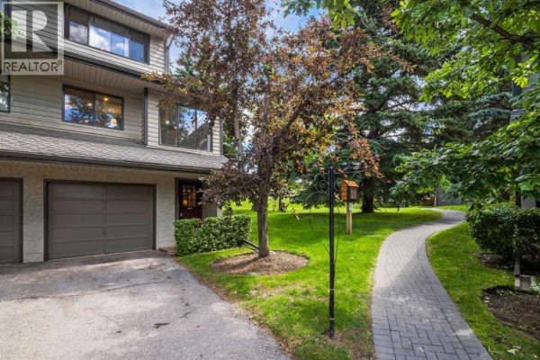 Side exterior of a townhouse with a paved walkway leading to the entrance. - 16, 140 Point Drive Nw, Calgary