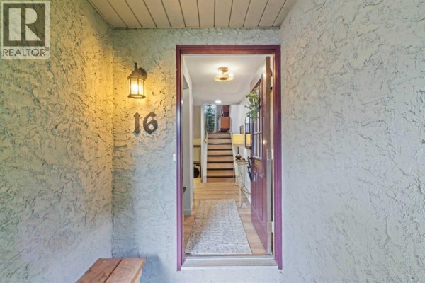 Open front door showing entryway with stairs and a bench. - 16, 140 Point Drive Nw, Calgary