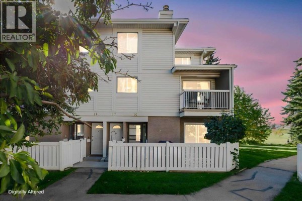 Exterior view of beige townhouse units at dusk with white picket fences. - 16, 3015 51 Street Sw, Calgary