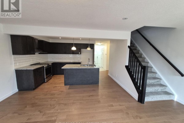 Open-concept living area with a kitchen, island, and carpeted stairs. - 16 - 125 Hollybrook Trail, Kitchener