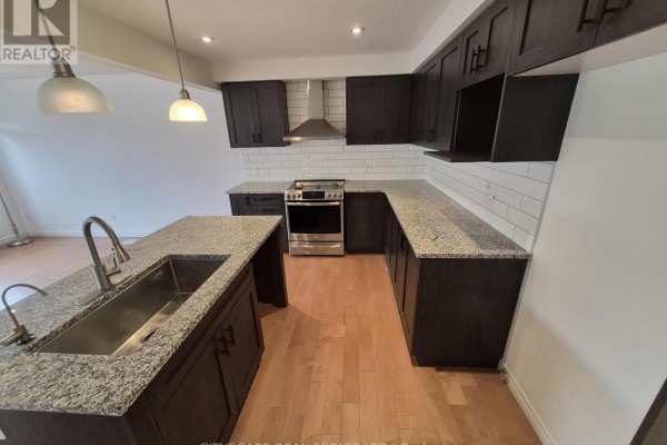 Kitchen island with a sink and granite countertop, surrounded by dark cabinetry. - 16 - 125 Hollybrook Trail, Kitchener