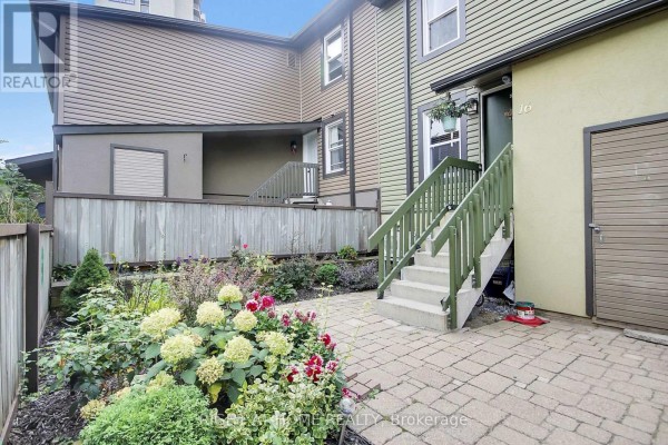 Stone patio with stairs leading to the front door of a townhouse, surrounded by garden beds. - 16 - 1250 Mcwatters Road N, Ottawa