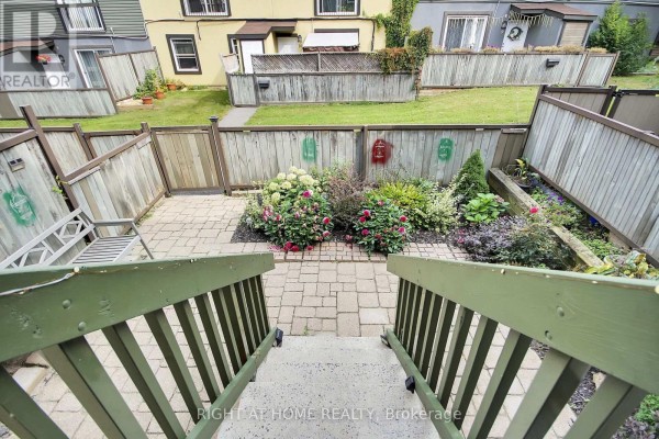 View from stairs looking down at a landscaped backyard with a stone patio, wooden fences, and garden. - 16 - 1250 Mcwatters Road N, Ottawa