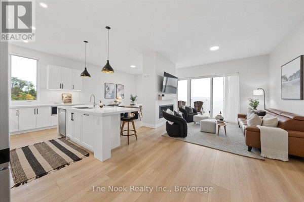 Open concept living and kitchen area with white cabinets, island, fireplace, and furniture. - 16 - 19 West Street N, Kawartha Lakes