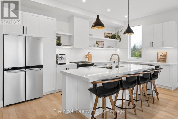 Modern white kitchen with stainless steel refrigerator, island with bar stools, and pendant lights. - 16 - 19 West Street N, Kawartha Lakes