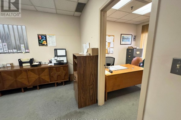 Another view of the office showing desk, wooden storage, and wall-mounted documents. - 16 - 3300 Steeles Avenue W, Vaughan