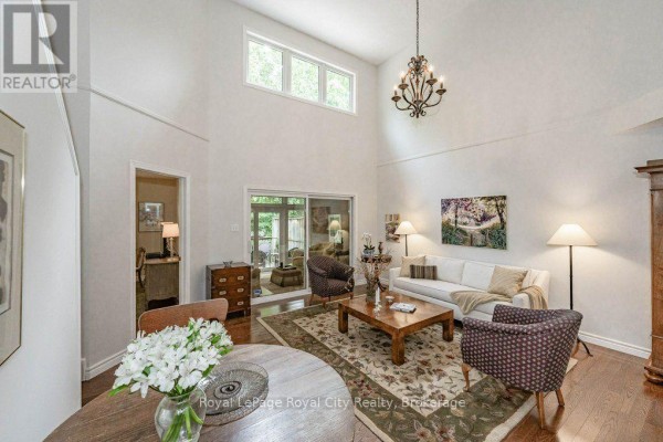 Living room with vaulted ceiling, chandelier, and large windows overlooking trees. - 16 - 784 Gordon Street, Guelph