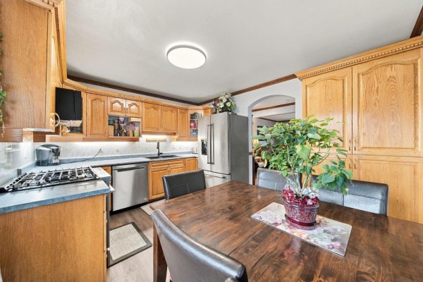 Kitchen and dining area with wooden table, stainless steel refrigerator, oak cabinets, and large plant. - 16 11735 89a Avenue, Delta