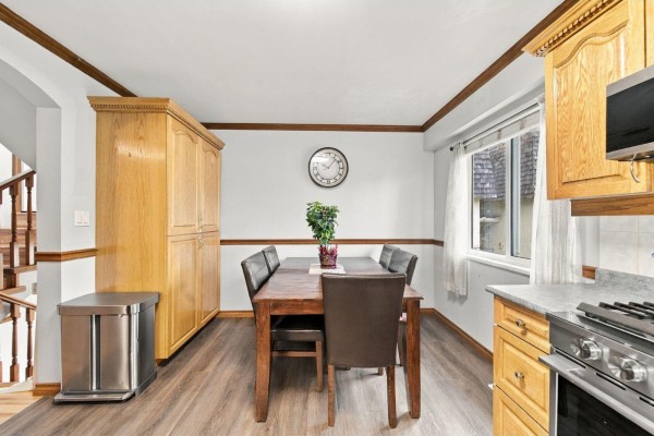 Dining area with wooden table and chairs, large oak cabinet, stainless steel trash can, and window. - 16 11735 89a Avenue, Delta