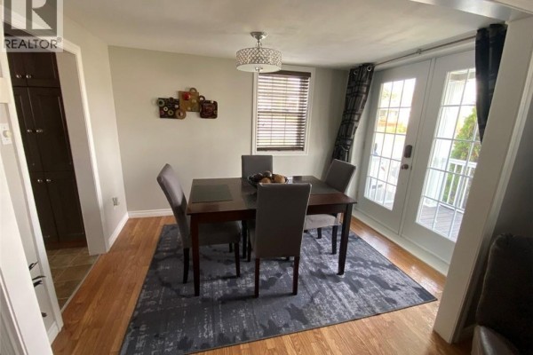Dining room with a dark wood table, grey chairs, hardwood floors, and double doors leading outside. - 16 46th Avenue, Edmundston