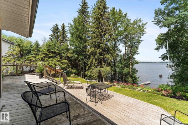 View of a wooden deck with outdoor furniture overlooking a lake surrounded by trees. - #16 53004 Rge Road 54a, Rural Parkland County