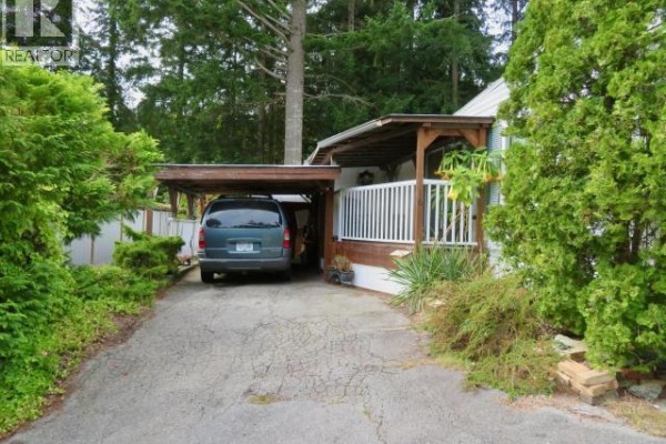 Driveway leading to a carport with a dark green minivan parked underneath. - 16-6263 Lund, Powell River