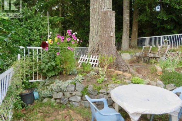 Backyard seating area with a round table, chairs, and a stone retaining wall. - 16-6263 Lund, Powell River