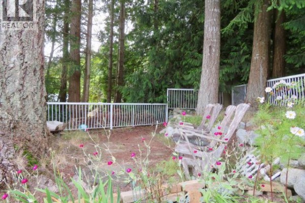 Wood chairs and a fire pit area in the backyard surrounded by trees and flowers. - 16-6263 Lund, Powell River