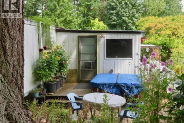Rear exterior of the mobile home with a covered hot tub and a small deck. - 16-6263 Lund, Powell River