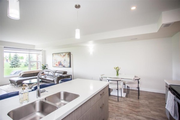 View from kitchen island showing dining area, living room, and backyard through window. - 16 865 Rathgar Avenue, Winnipeg