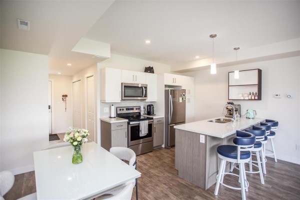 Kitchen and dining area with island, bar stools, white table, and stainless steel appliances. - 16 865 Rathgar Avenue, Winnipeg
