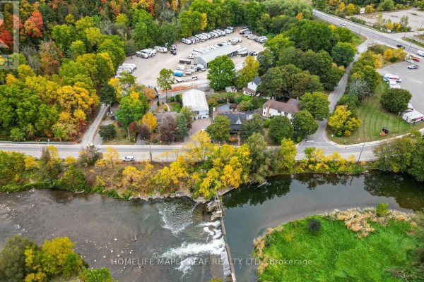 Aerial view of the property along a river, featuring buildings, a paved lot with RVs, and autumn foliage. - 16 Adamson Street, Halton Hills